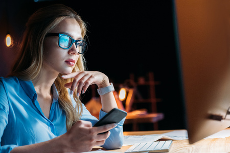 businesswoman using smartphone while working late in officeの写真素材