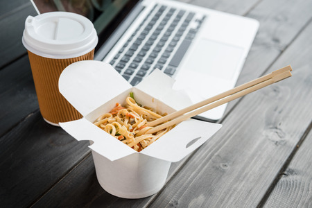 close up of noodle with chopsticks and coffee to go with laptop