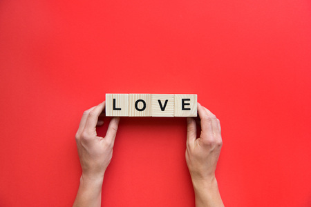 Human hands holding wooden cubes with love sign isolated on red backgroundの写真素材