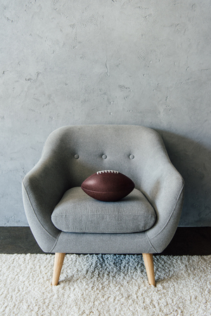 american football ball on grey textile armchair at empty roomの写真素材