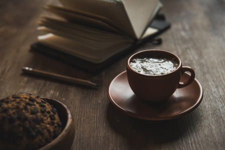 Close-up view of open notebook with pencil, cup of coffee and chocolate chip cookie on wooden tableの写真素材