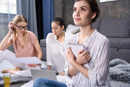 young woman dreaming and holding notebook while her colleagues working at homeの写真素材