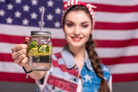 smiling woman showing detox drink in hand with American flag on backgroundの写真素材