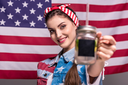 smiling woman showing detox drink in hand with American flag on backgroundの写真素材