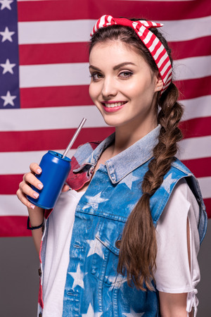 smiling woman holding drink in hand with american flag behindの写真素材