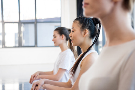 young women in sportswear meditating at yoga classの写真素材