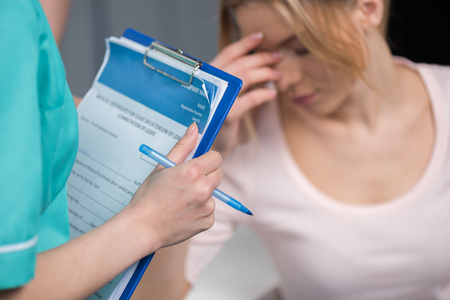 nurse holding clipboard and pen while upset patient sitting behindの写真素材