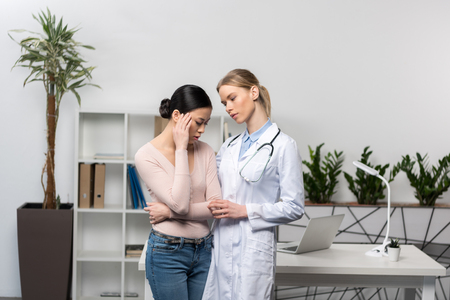 doctor with stethoscope talking with upset patient suffering from headacheの写真素材