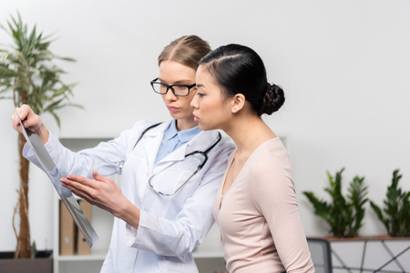 doctor and patient looking at x-ray image while standing in hospitalの写真素材