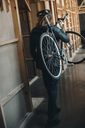 stylish young man with long hair walking and carrying bicycle on shoulderの写真素材