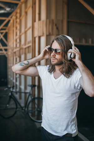 young long haired man adjusting headphones and looking awayの写真素材