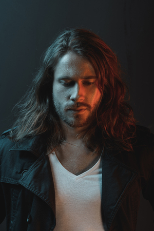 handsome stylish bearded young man with long hair looking down in studio