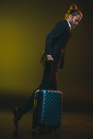 stylish caucasian man in suit walking with suitcaseの写真素材