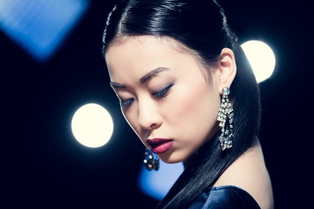 sensual asian woman posing in diamond earrings at event with spotlightsの写真素材