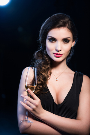 seductive young woman in evening gown holding glass of champagne looking at cameraの写真素材