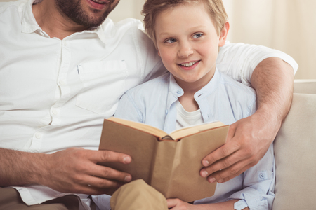 father and little son reading book at homeの写真素材