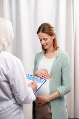 doctor writing down pregnant woman complaints during medical consultationの写真素材
