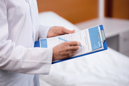 doctor writing diagnosis in clipboard at hospitalの写真素材