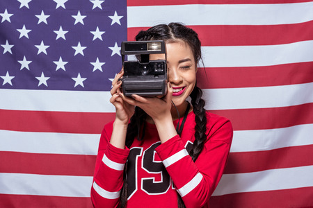asian woman holding retro photo camera with american flag behindの写真素材