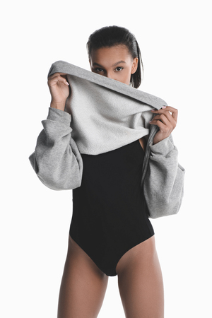 african american girl posing in black bodysuit and hiding face with grey sweaterの写真素材