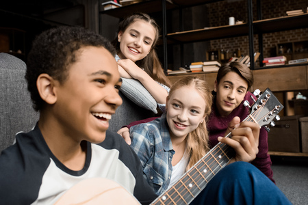 african american boy playing acustic guitar while his friends listening at homeの写真素材