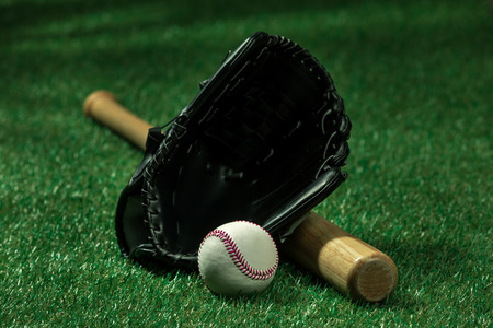 baseball bat, glove and ball lying on green grass