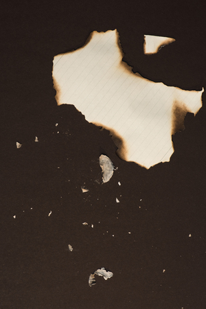 burned pieces of empty writing paper sheet isolated on blackの写真素材