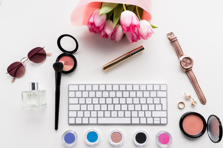 top view of computer keyboard, various cosmetics, accessories and bouquet of pink tulips