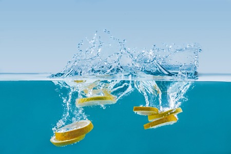 fresh lemon slices falling into water with splashes