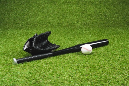 black baseball bat with leather glove and ball on green grassの写真素材