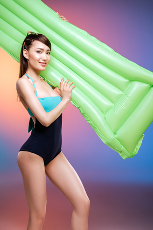 young woman in swimsuit posing with swimming mattress and smiling at cameraの写真素材