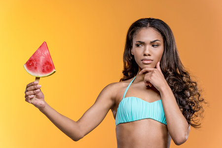 african american girl in swimwear holding watermelon pieceの写真素材