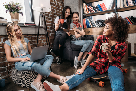 Smiling young women sitting together with laptop and coffee cupsの写真素材