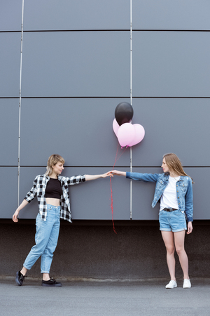 happy lesbian couple holding hands with air balloons outdoorsの写真素材