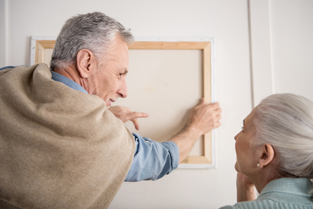 wife helping husband hanging picture on wall at new homeの写真素材