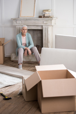 senior woman having rest on fireplace after unpacking boxesの写真素材