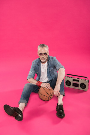 senior man sitting on floor with tape recorder and basketball ballの写真素材