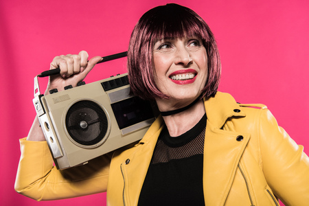 stylish senior woman holding tape recorder isolated on pinkの写真素材