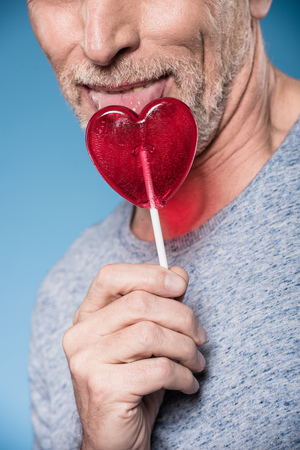 elderly man licking lollipop in form of heartの写真素材
