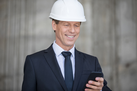 middle aged businessman in hard hat using smartphoneの写真素材