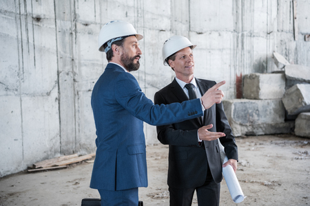 professional mature architects with blueprint working at construction siteの写真素材