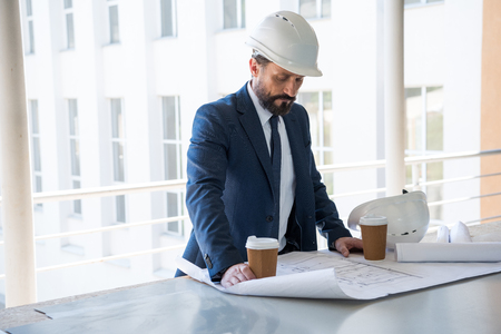aged architect in suit looking at blueprints at construction areaの写真素材