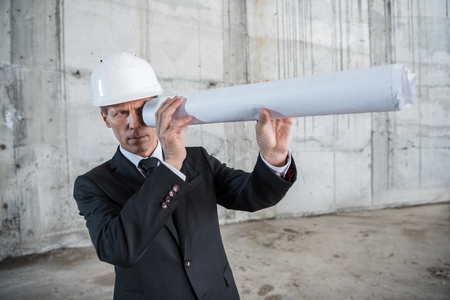 middle aged architect holding rolled blueprint while working at construction siteの写真素材