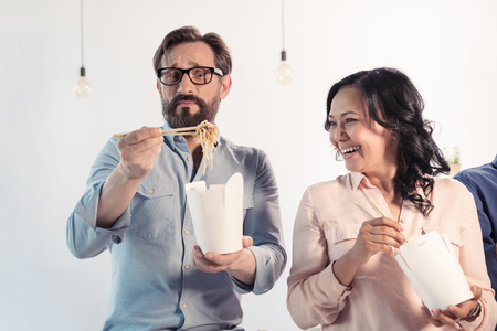 aged business colleagues eating asian food with chopsticks in officeの写真素材