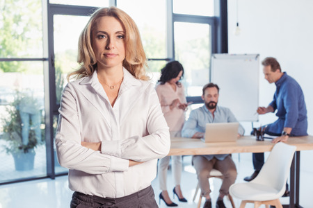 blonde businesswoman standing with crossed arms and looking at cameraの写真素材