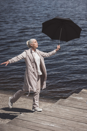 elderly woman walking with umbrella on riverside at daytimeの写真素材