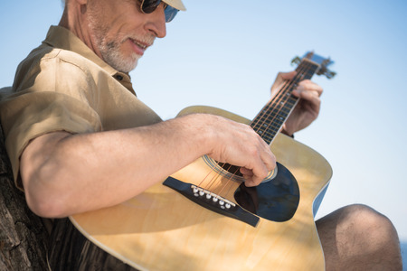 senior man in eyeglasses playing guitar outdoorsの写真素材