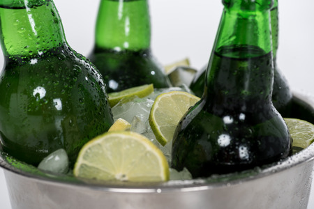 Close-up view of ice cubes, lemon slices and green beer bottles in bucket isolated on whiteの写真素材