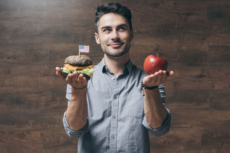 young man holding red apple and delicious hamburgerの写真素材