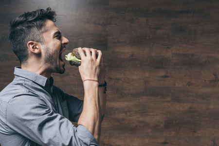 hungry young man biting delicious hamburgerの写真素材